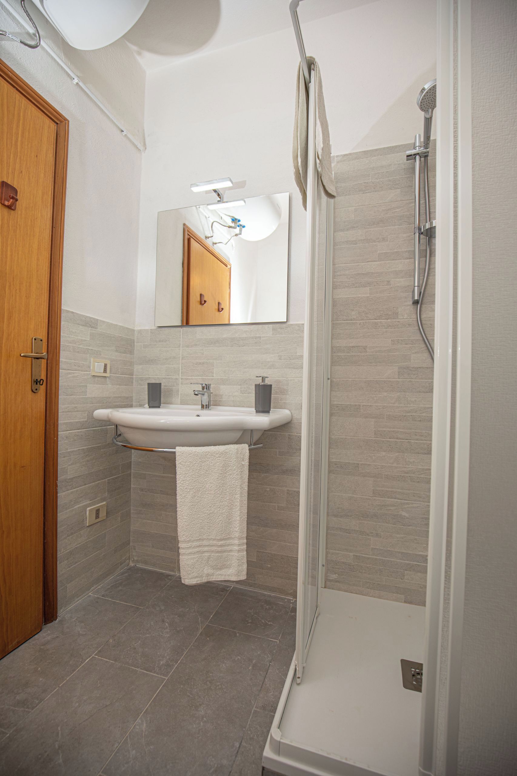 A modern bathroom with a wooden door, a sink with a mirror above it, and a shower area.