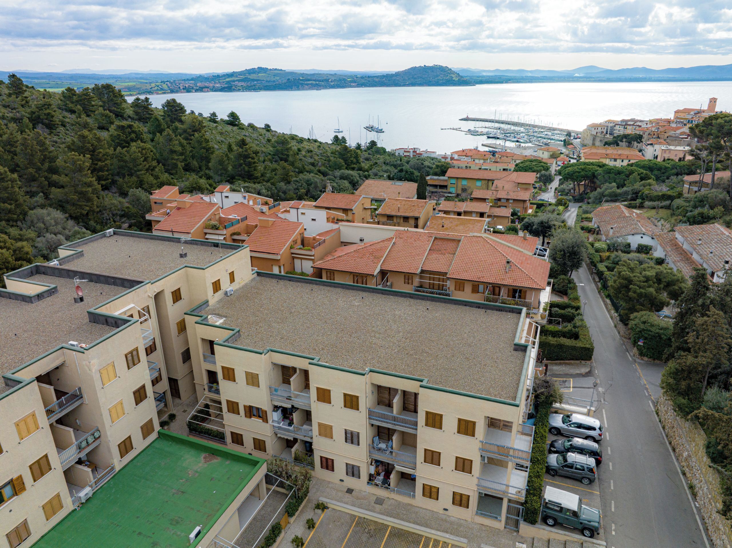 Una cittadina costiera con edifici a tetti in terracotta, un porto turistico e vista sul mare.