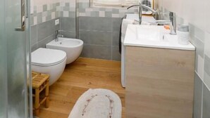 A bathroom with a glass shower enclosure, a toilet, a bidet, a sink, and a mirror.