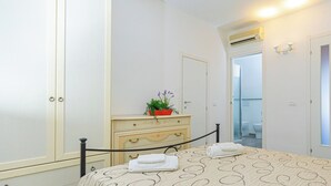 Une chambre d’hôtel avec un lit, une commode agrémentée d’une plante, un miroir et une porte donnant sur une salle de bain.