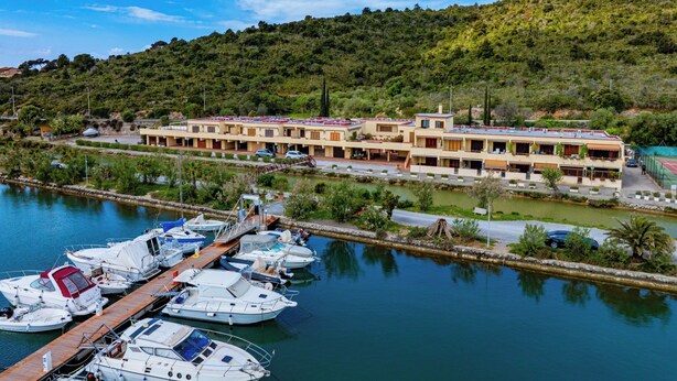 Un hôtel situé sur la côte, composé de plusieurs bâtiments, avec un port de plaisance rempli de bateaux et une colline en arrière-plan.
