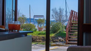 Une vue depuis une fenêtre donnant sur une zone côtière, avec un escalier en bois menant à l’extérieur.
