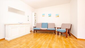 Ein geräumiges Wohnzimmer mit Holzboden, einem weißen Schrank, einer Couch mit Kissen und einem Sessel.