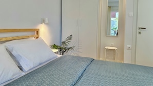 A bedroom with a bed, a bedside table, a mirror, and a wardrobe. - Modern Seaside Home with Private Patio + Parking - Blue Zone Homes (Olimpiaki Akti)