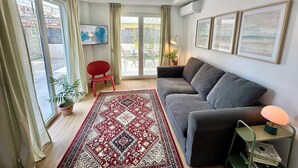 A modern living room with a grey sofa, red chair, and a patterned rug. - Modern Seaside Home with Private Patio + Parking - Blue Zone Homes (Olimpiaki Akti)