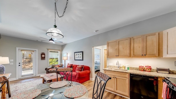 A modern kitchen with wooden cabinets, a dishwasher, and a dining area with a glass table and chairs. - Alpine Village Condo E| Location, Location, Location, Across From RIver and Tubing!! (Helen)