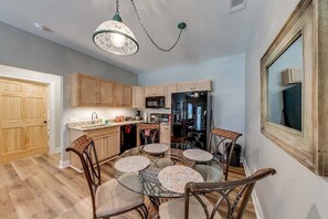 A kitchen with wooden cabinets, a refrigerator, a microwave, and a dining area with a glass table and chairs.