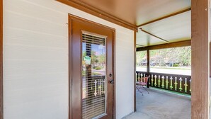 A covered porch with a brown door, a metal grill, and a chair. - Alpine Village Condo E| Location, Location, Location, Across From RIver and Tubing!! (Helen)