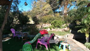 Une aire de jeux avec un toboggan, des balançoires et une table avec des chaises.