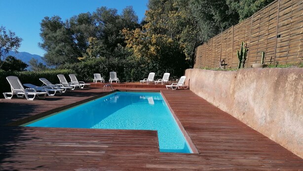 Une piscine rectangulaire dotée d’une terrasse en bois et de chaises longues blanches.