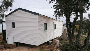 Une maison mobile blanche, dotée d’un toit à pignon, d’une petite fenêtre sur le côté et d’un réservoir d’eau en métal à l’avant.