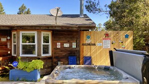 A wooden cabin with a hot tub, a table, and chairs outside.