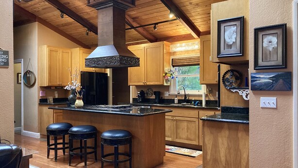 A kitchen with wooden cabinets, a central island with stools, a large stove, and framed artwork on the walls.