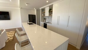 Une cuisine moderne dotée d’un grand îlot central, de meubles blancs et d’appareils électroménagers intégrés.