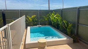 Une piscine rectangulaire dont les bords sont recouverts de carreaux, entourée d’une clôture métallique et de diverses plantes tropicales.