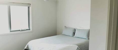 A bedroom with a bed, a ceiling fan, a window, and a door.