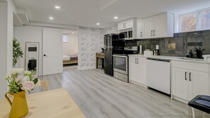 A modern kitchen with white cabinets, a black refrigerator, a microwave, and a dishwasher. There is a wooden dining table with a yellow vase of flowers. - TorontoGEM: 20 mins to Downtown,10 mins to Airport (Toronto)