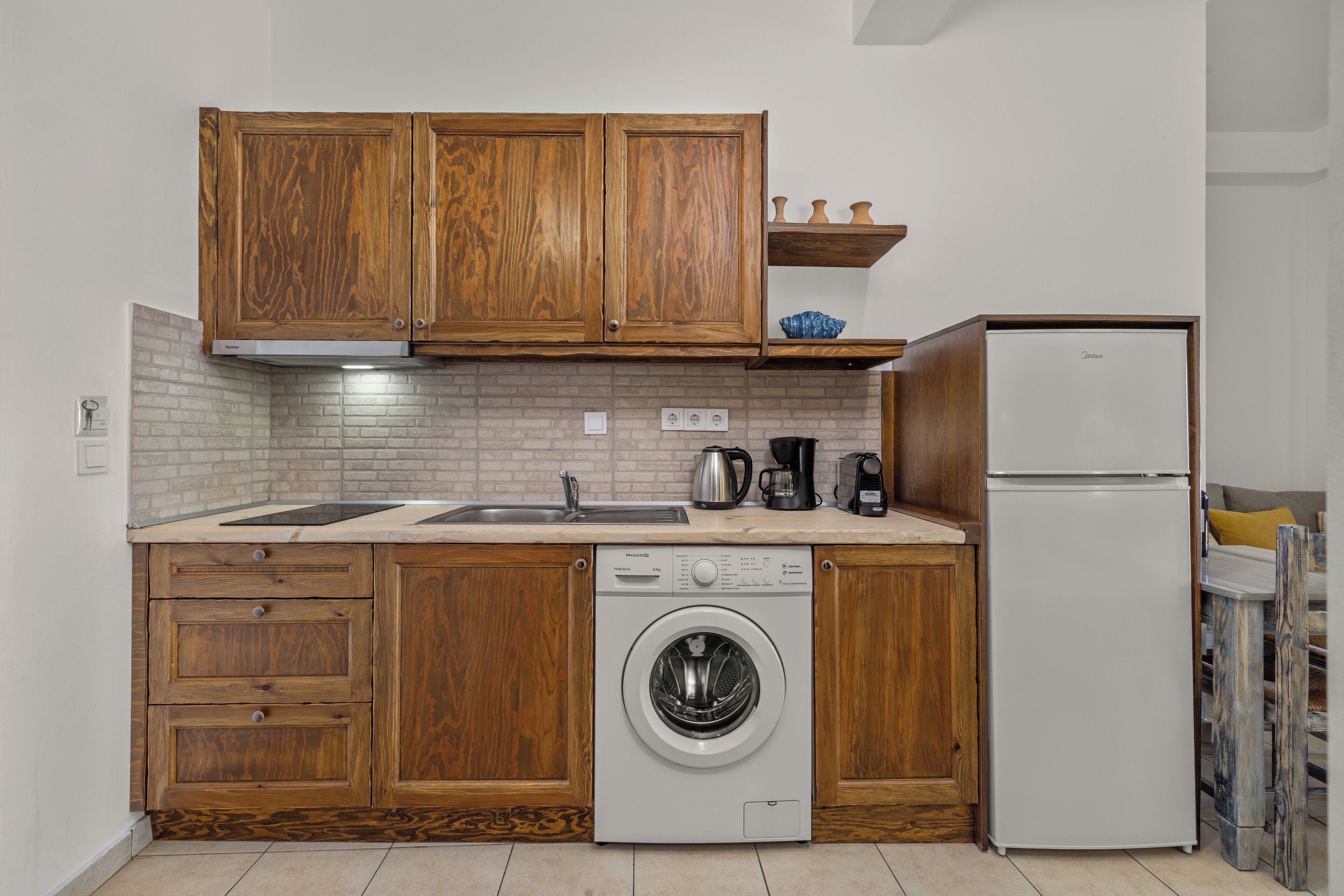 A compact kitchen with wooden cabinets, a built-in washing machine, a refrigerator, and a coffee maker.