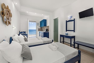 A hotel room with two beds, a desk, a TV, and a view of the sea.