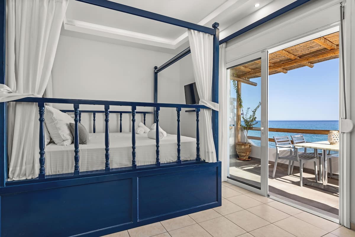 Un dormitorio con cama con dosel, ropa de cama blanca y vista al mar a través de un ventanal corredero.