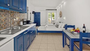 A compact kitchen with blue cabinets, a tiled backsplash, and a dining area with a blue table and chairs. - ammos stegna studios  (Rhodes)