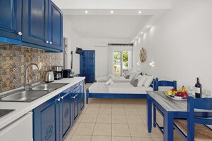 Cocina compacta con armarios azules, salpicadero de azulejos y comedor con mesa y sillas azules.