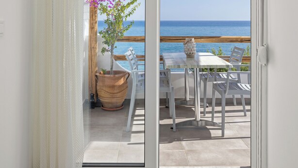 A room with a sliding glass door leading to an outdoor patio with a table, chairs, and a potted plant. - ammos stegna studios  (Rhodes)