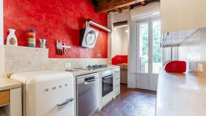 A kitchen with a white refrigerator, stove, and dishwasher. There is a red wall and a window with a view of greenery. - Pepi 64 in Firenze With 2 Bedrooms and 1 Bathrooms (Florence)