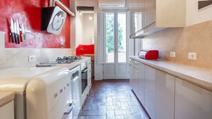 A kitchen with white cabinets, a red wall, and a window leading to a garden. - Pepi 64 in Firenze With 2 Bedrooms and 1 Bathrooms (Florence)
