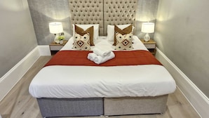 A neatly made bed with a red blanket, two nightstands with lamps, and a tufted headboard. - THE FORBURY  (Reading)