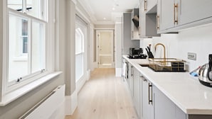 A modern kitchen with white cabinetry, a stainless steel sink, and a built-in oven. - THE FORBURY  (Reading)