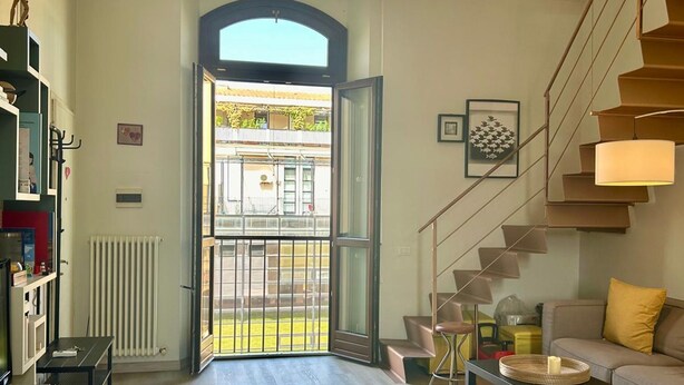 A modern living room with a staircase, a sofa, a coffee table, and a view of the outside. - La Corte di San Domenico (Pisa)