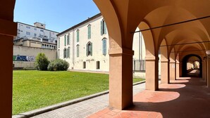 A covered walkway with arches, a grassy area, and a building with windows. - La Corte di San Domenico (Pisa)