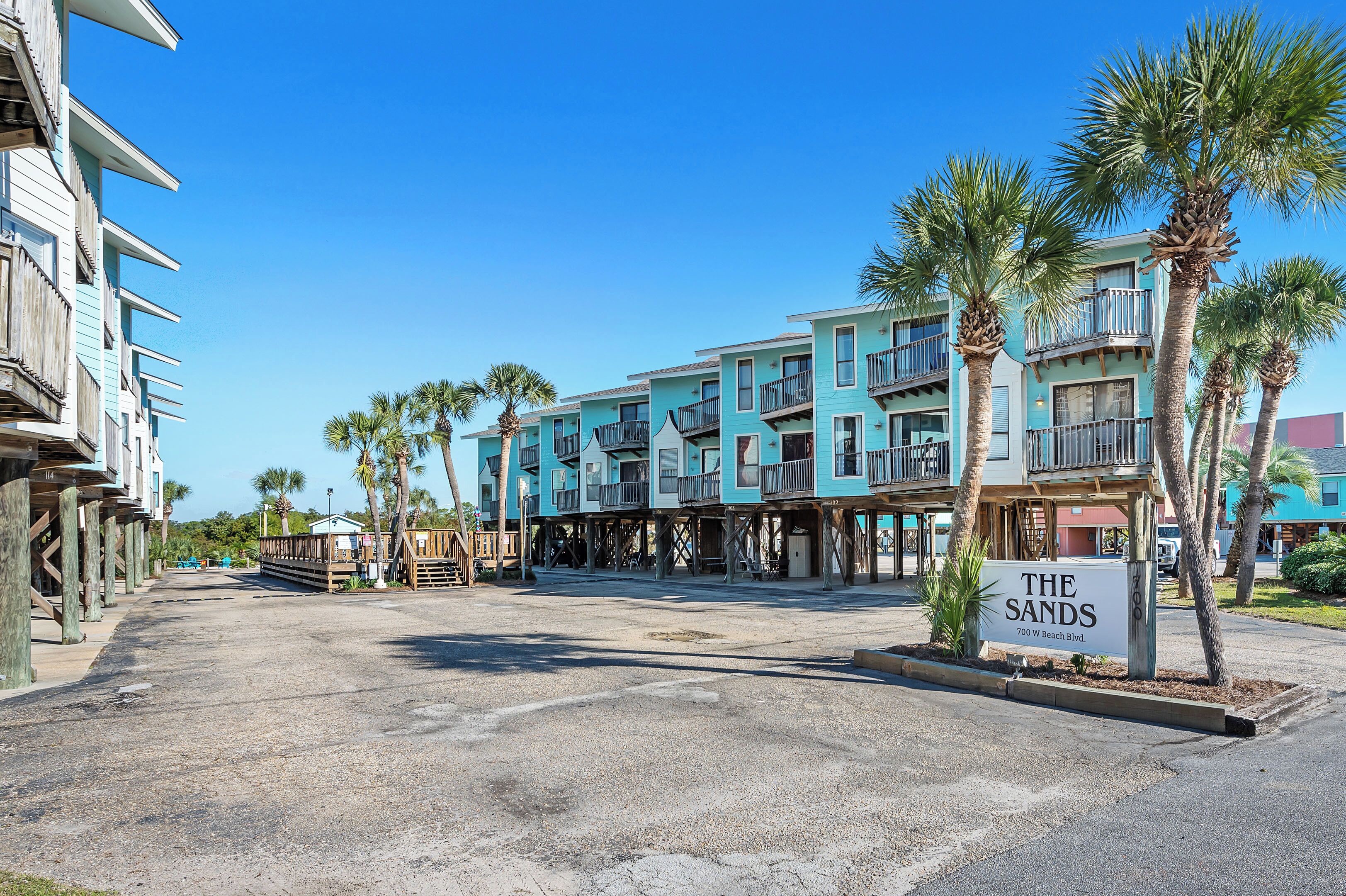 A beachfront hotel with a sign reading "The Sands" at 700 W Beach Blvd. It features multi-story buildings with balconies and palm trees.