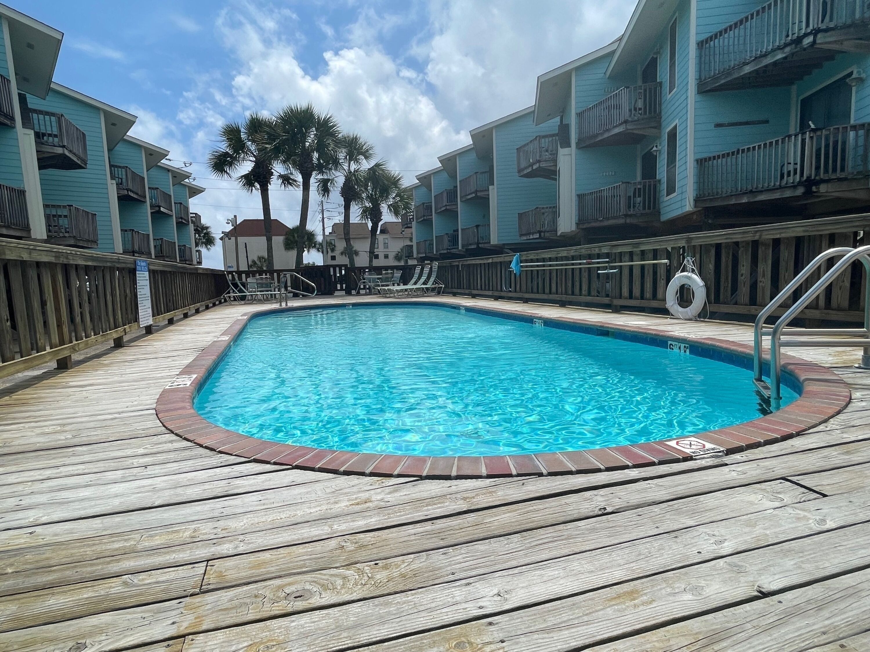 A swimming pool with a wooden deck, surrounded by multi-story buildings with balconies.