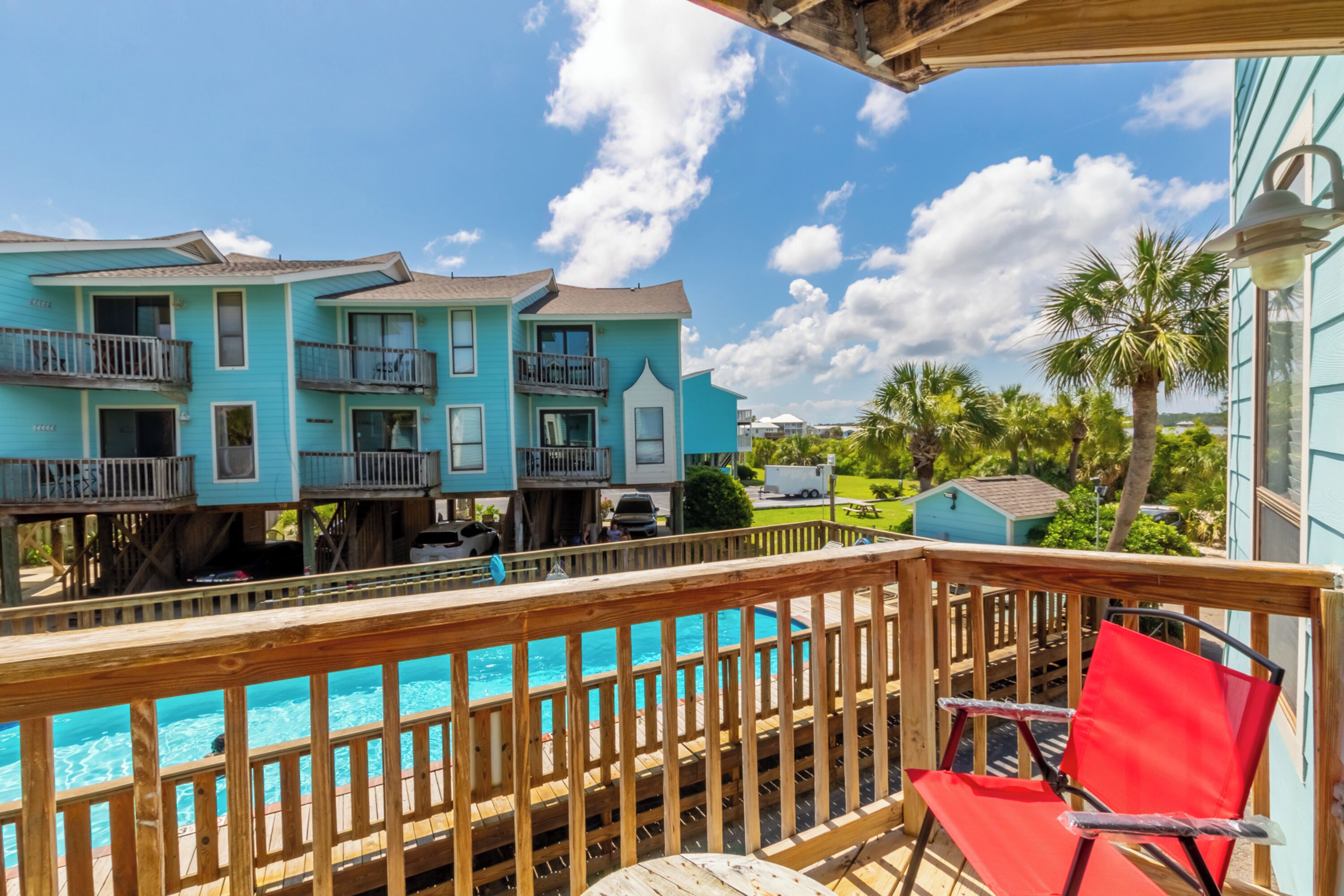 A turquoise two-story building with balconies, a wooden deck, and a pool.