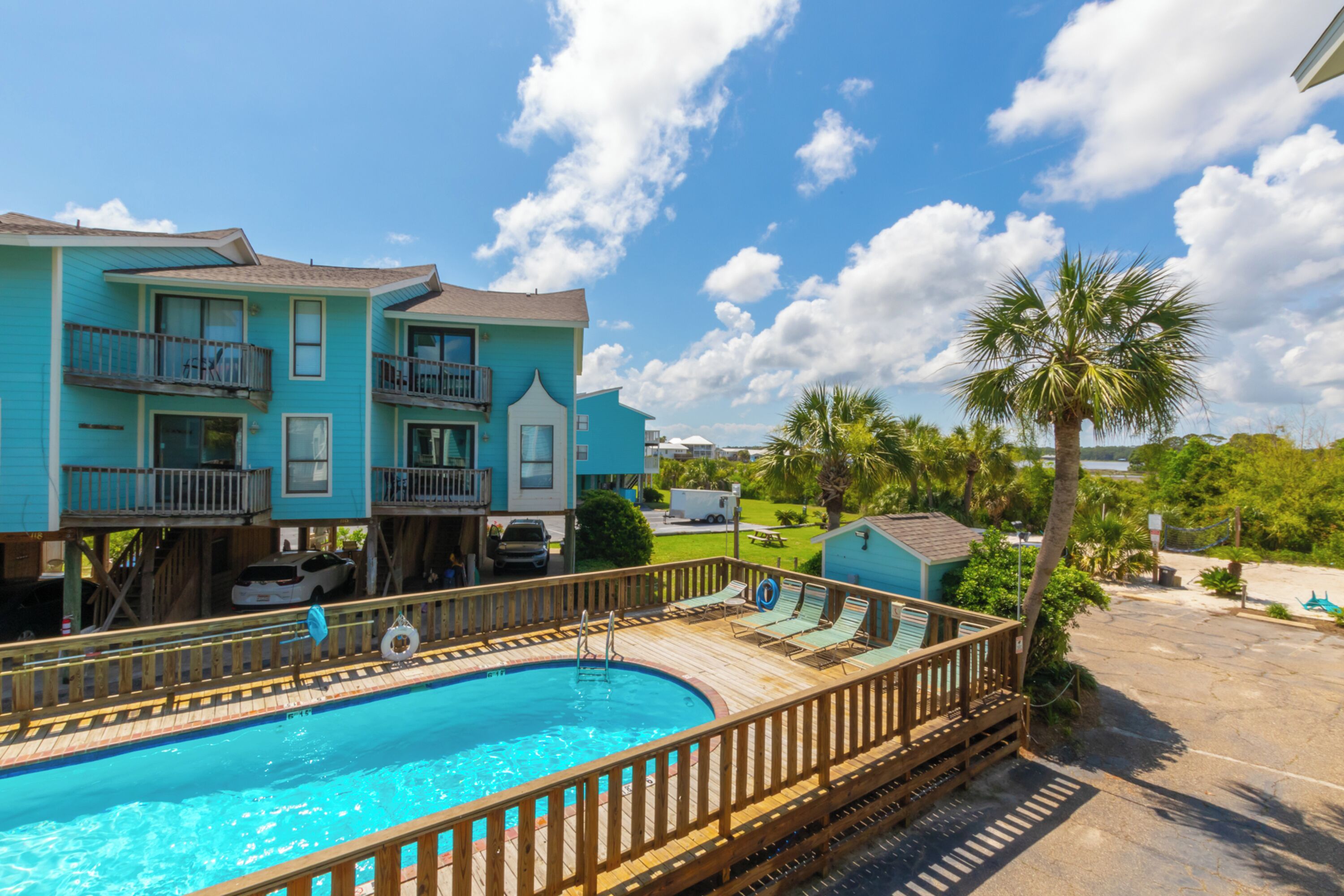 A pool area with a wooden deck and lounge chairs, surrounded by a two-story building with balconies.