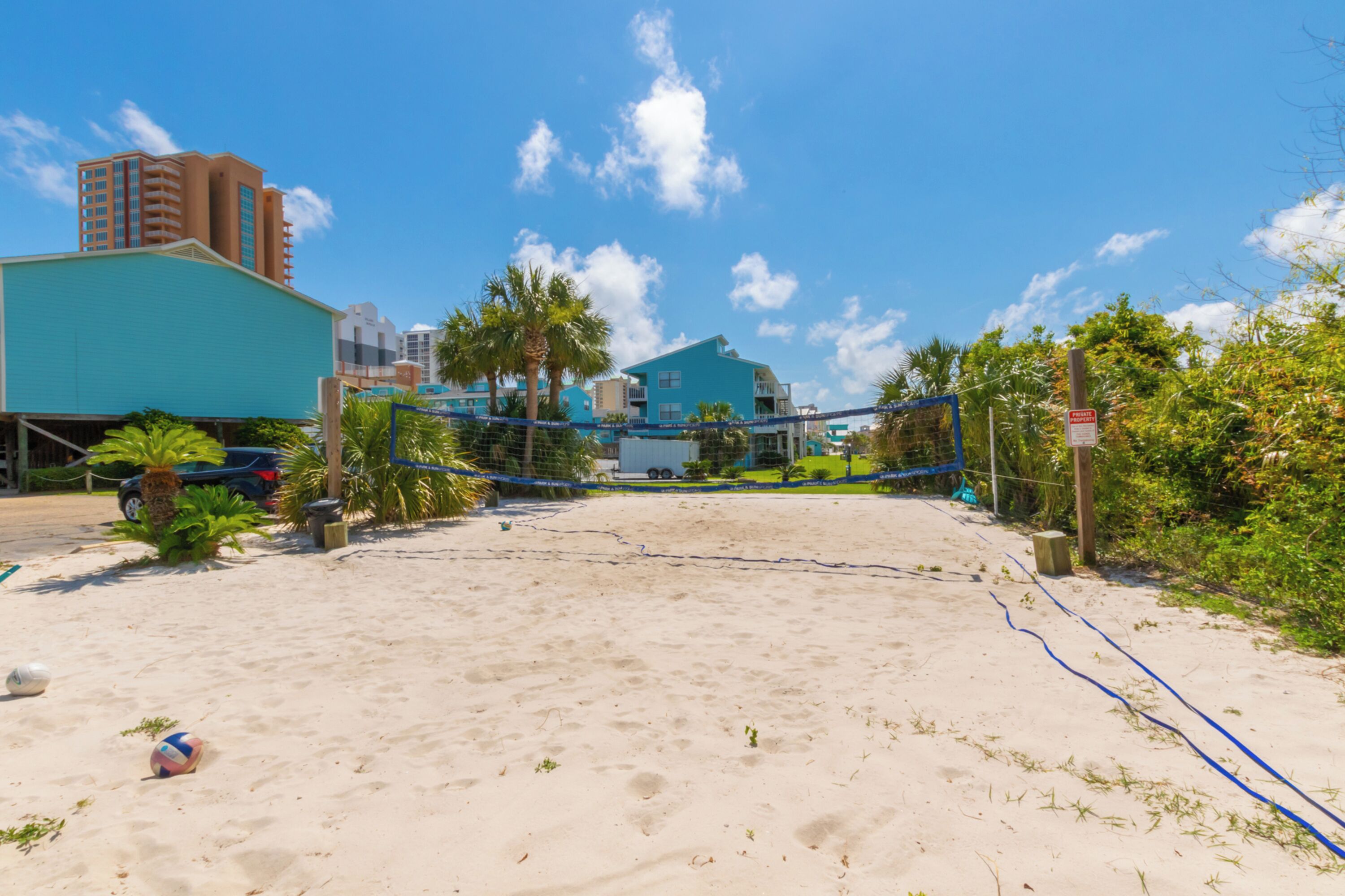 Una cancha de voleibol de playa con red, palmeras y edificios al fondo.
