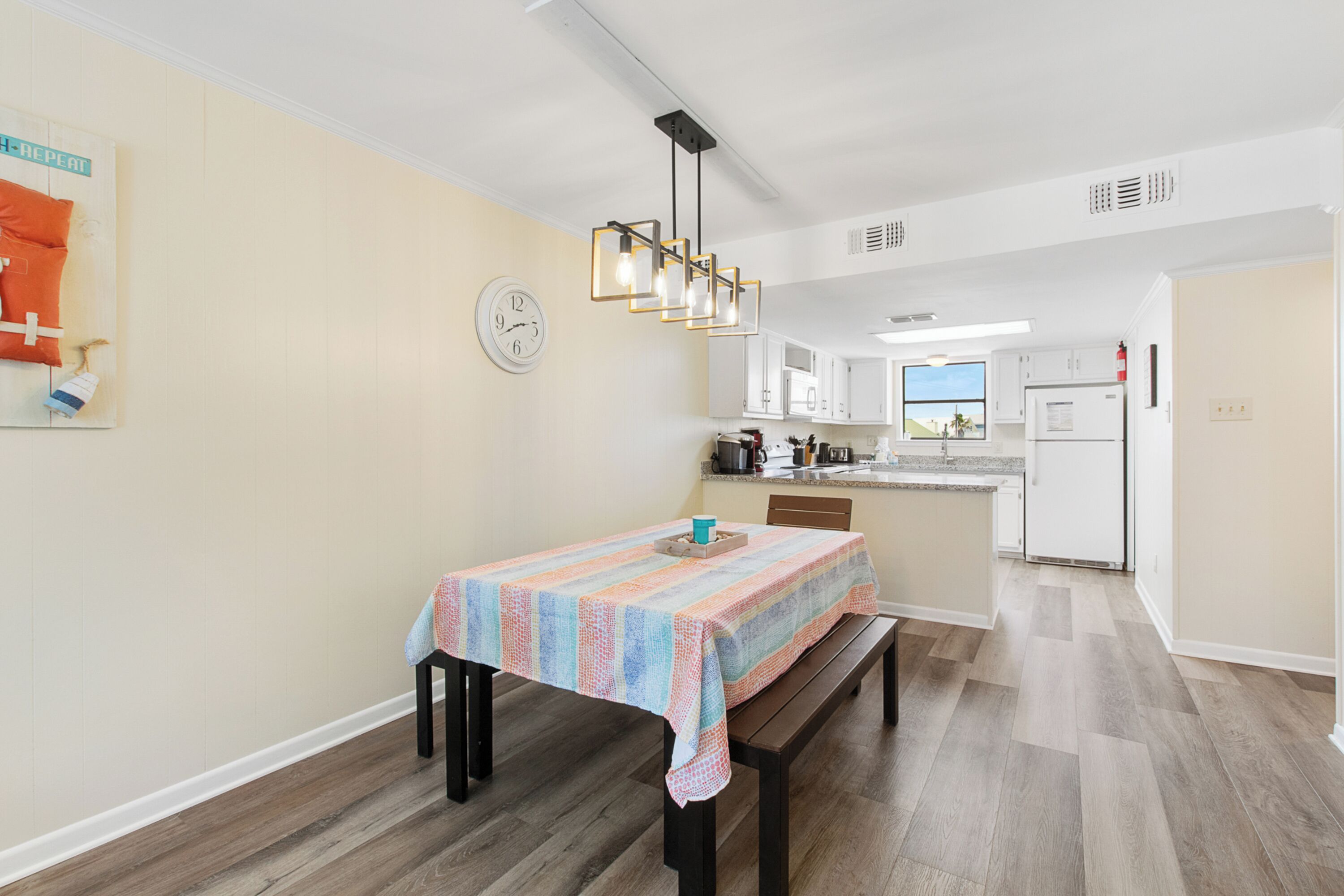 A modern kitchen with white cabinets, a central island, and a dining area with a wooden bench and table.