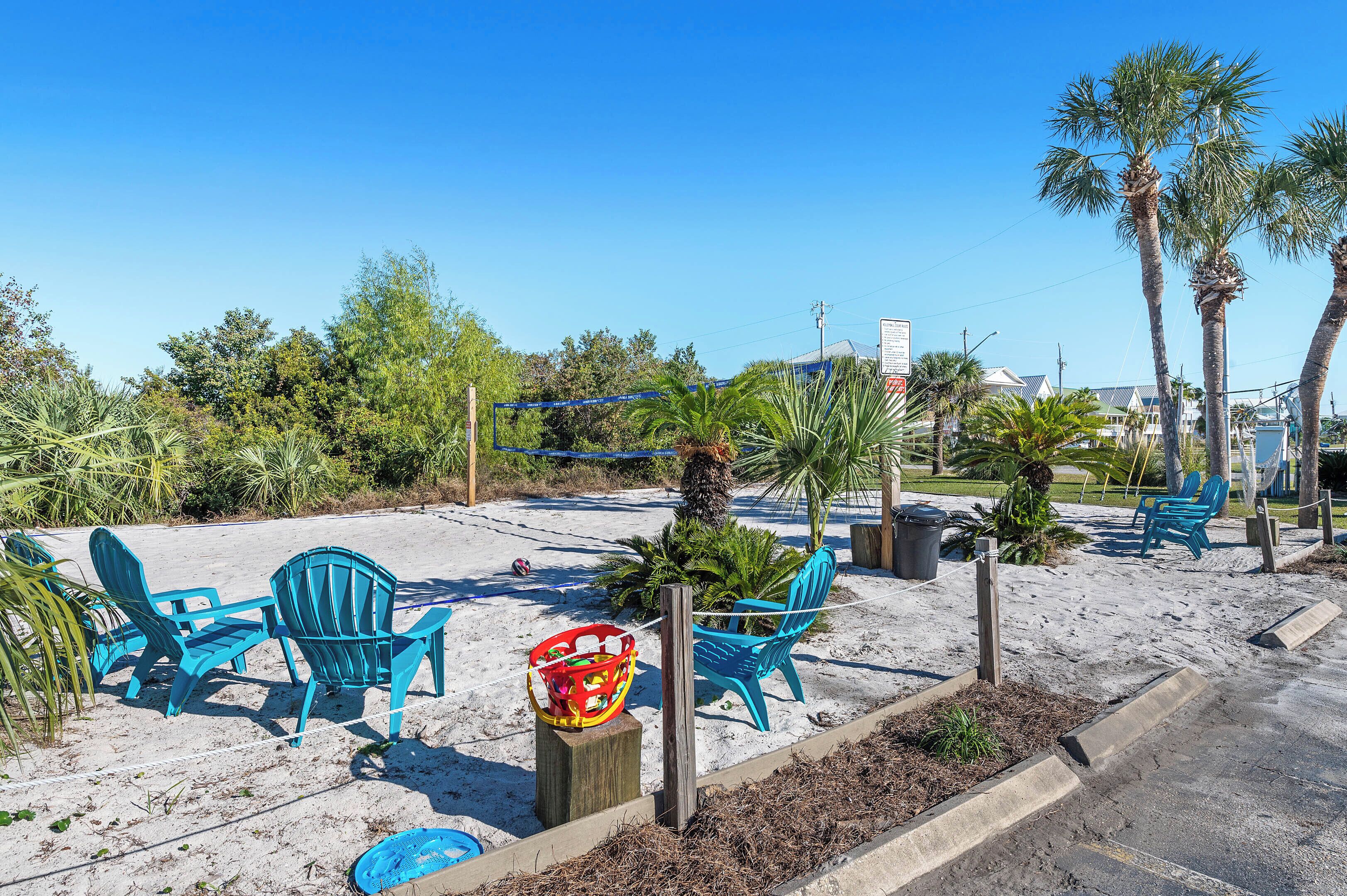 Un espace aménagé au bord de la plage, avec des chaises bleues et un panier rouge fixé sur un poteau en bois.