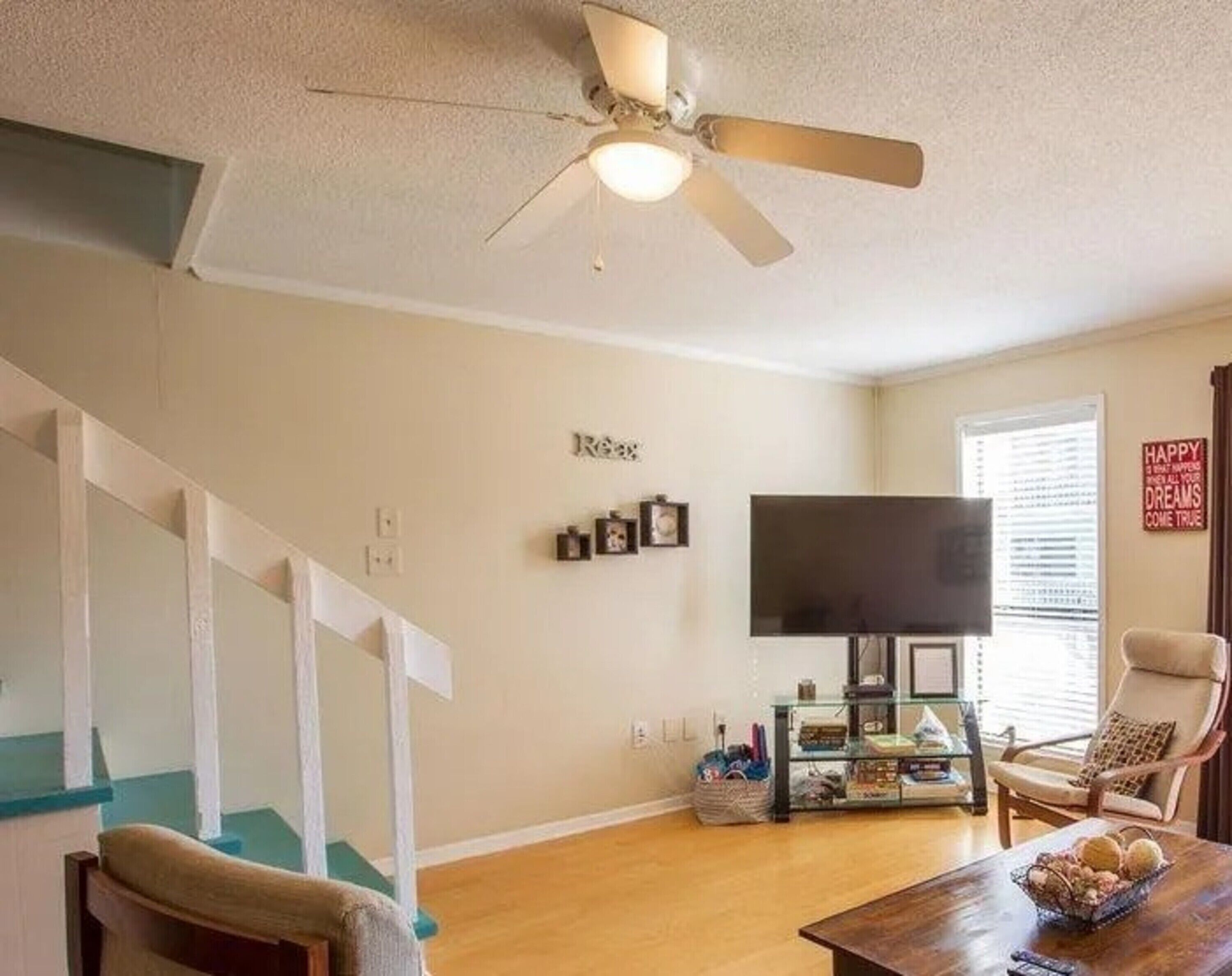 A living room with a ceiling fan, a flat-screen TV, a glass coffee table, and a chair.