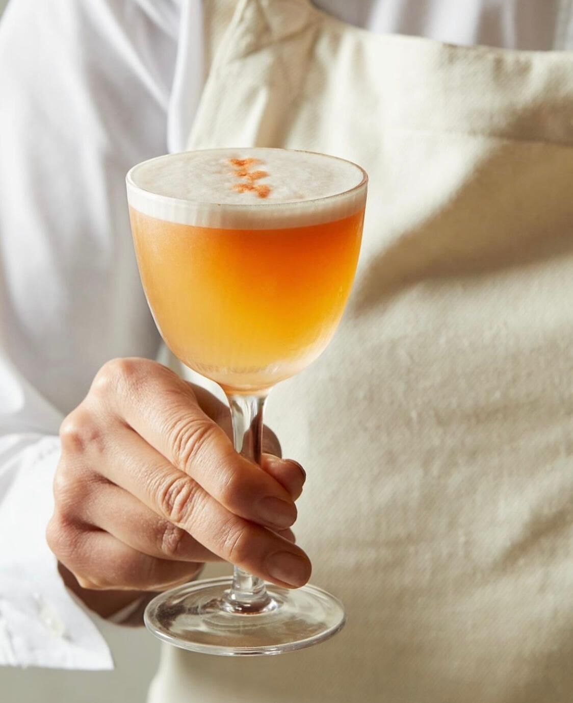 A person holding a glass of a layered beverage with a frothy top.
