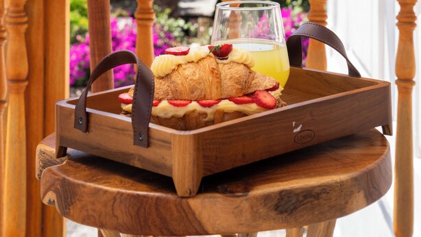 Ein Holzhocker mit einer Ablage, auf der ein Croissant-Sandwich und ein Glas Orangensaft stehen.
