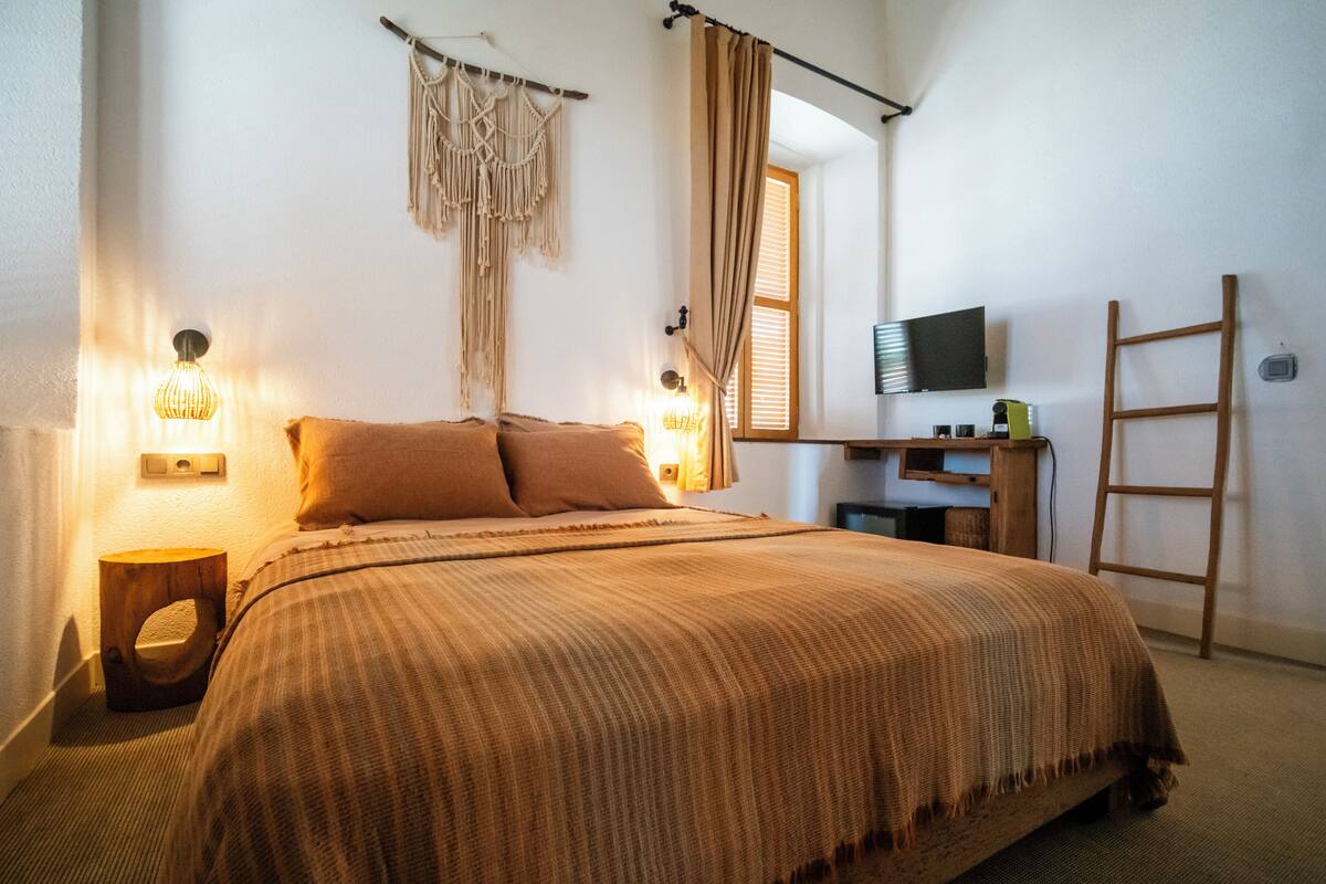 Quarto com cama grande, escrivaninha com cadeira, televisão e escada.