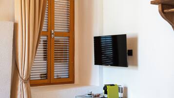 A room with a wooden door, beige curtains, a mounted TV, a desk with a chair, and a basket on the floor.