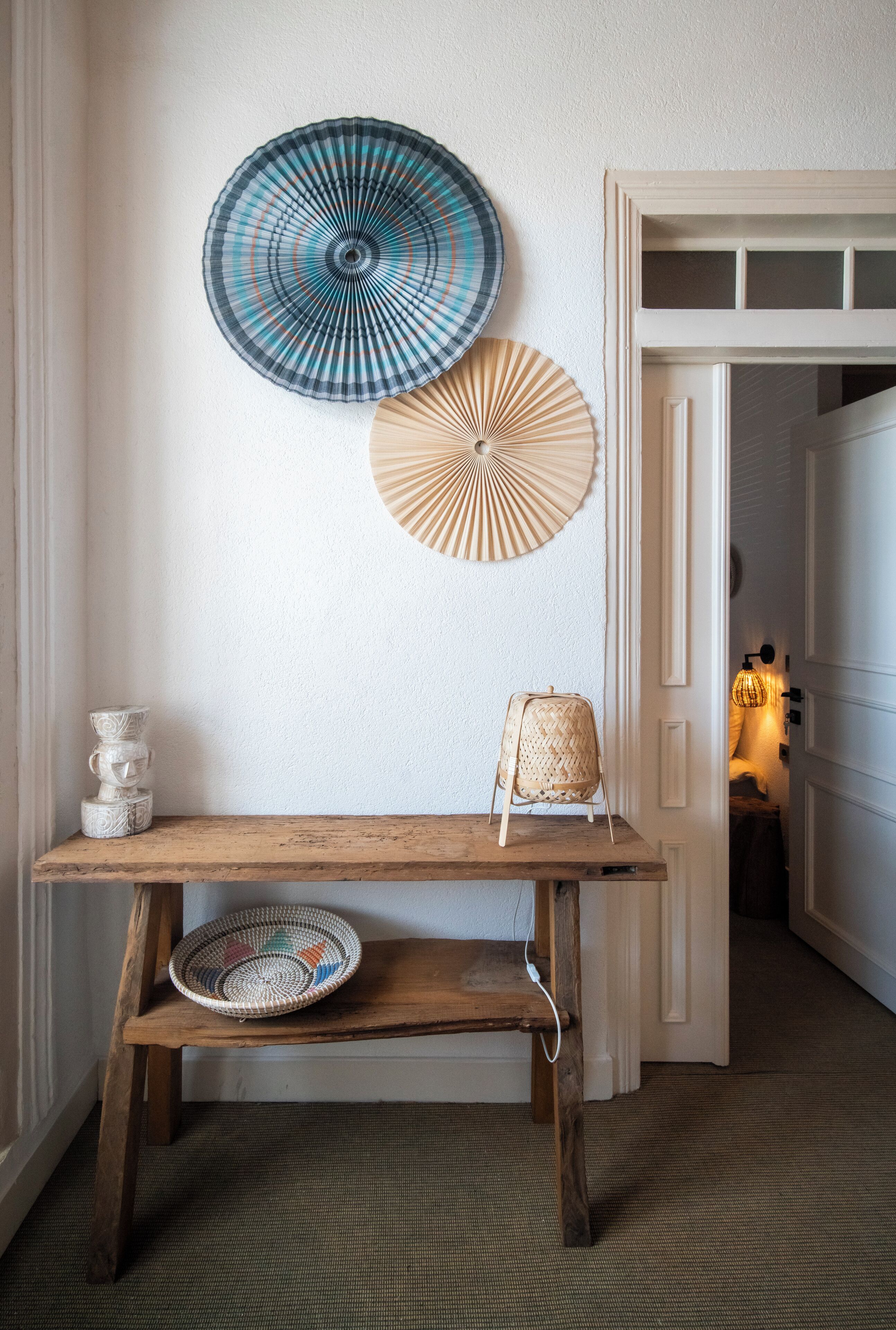 A hallway with a wooden bench, two wall-mounted fans, and a door leading to another room.