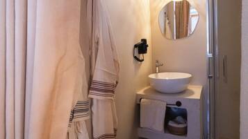 Un baño con lavamanos blanco, espejo y ducha. Hay toallas colgadas en un perchero y una alfombra en el suelo.