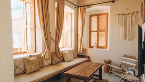Ein gemütliches Zimmer mit einer Holzbank, einer gepolsterten Sitzbank, einem kleinen Holztisch, einem Stuhl und einer Wanddekoration aus Makramee.