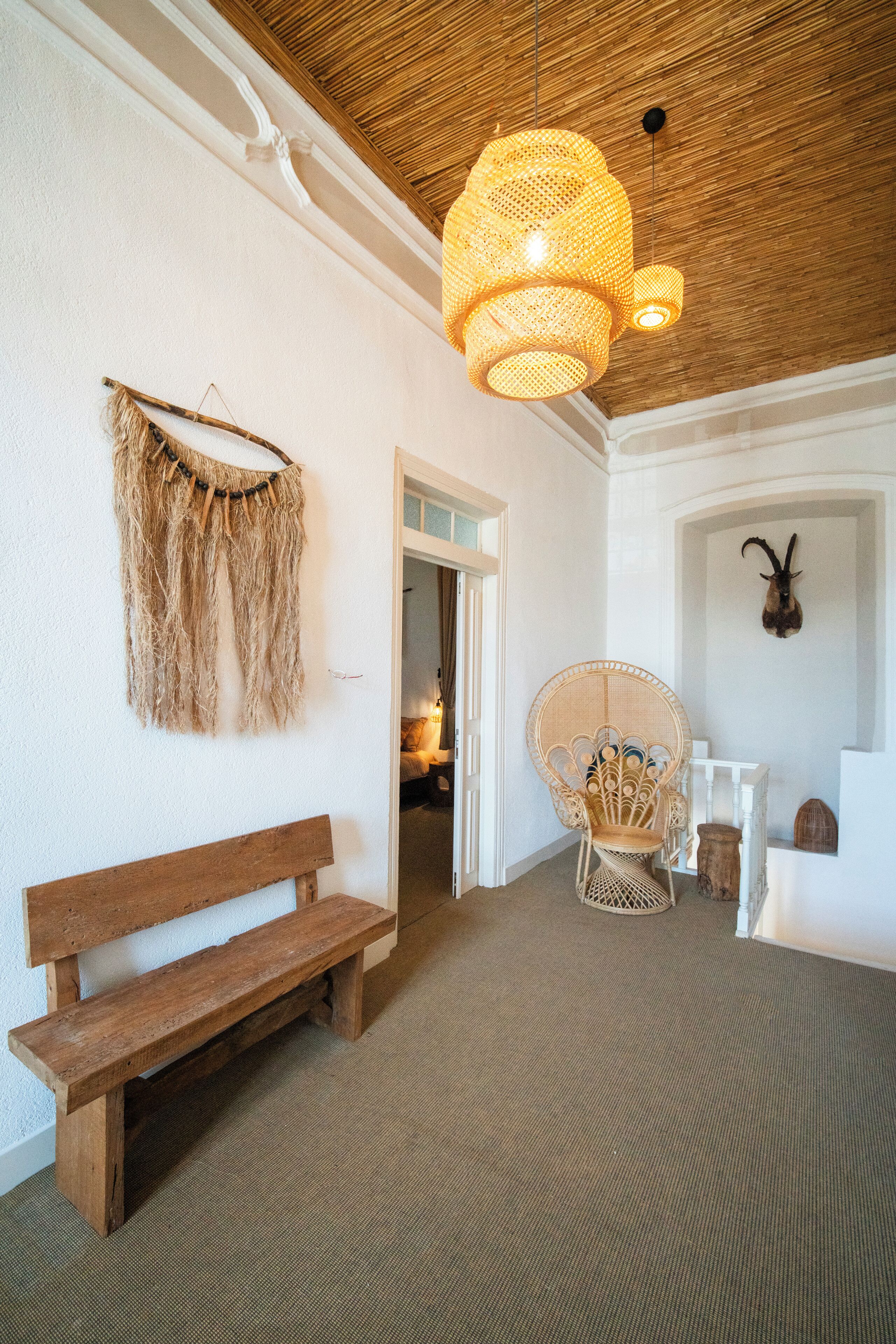A room with a wooden bench, a woven chair, a wall-mounted decorative piece, and a ceiling light fixture.