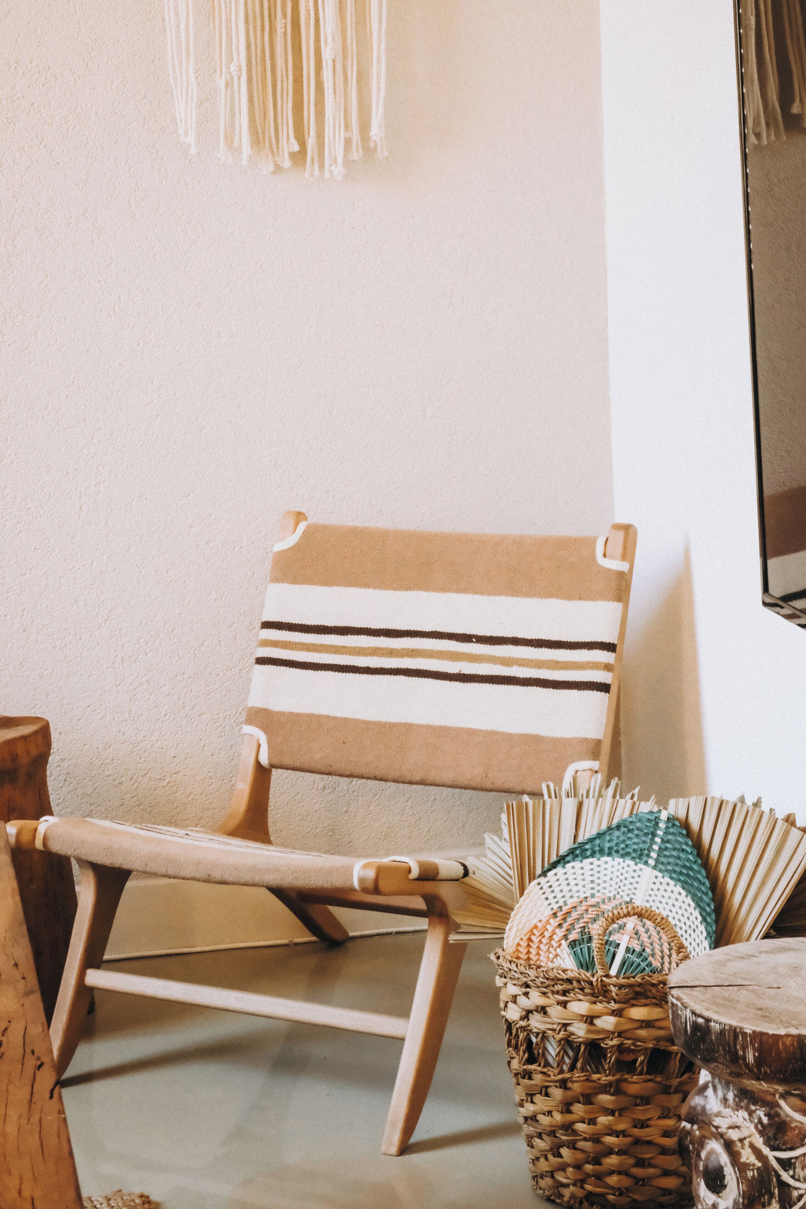 A wooden chair with a striped cushion, a woven basket, and a woven pillow on a plain wall.